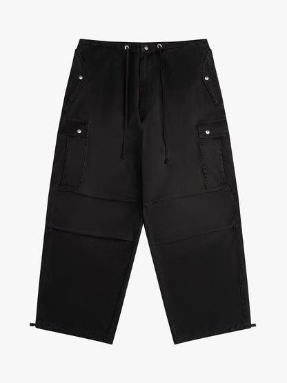 Washed black wide-leg parachute pants with a drawcord waist, snap-flap cargo pockets and toggled hems, front view