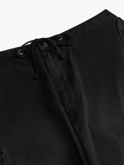 Close-up of the black drawcord threaded through metal eyelets at the waist of the washed black parachute pants