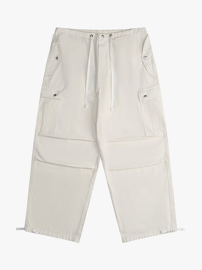 Off-white wide-leg parachute pants with a white drawcord waist, snap-flap cargo pockets and toggled hems, front view