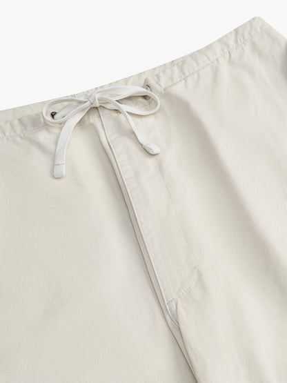 Close-up of the white drawcord tied in a bow through metal eyelets at the waist of the off-white parachute pants
