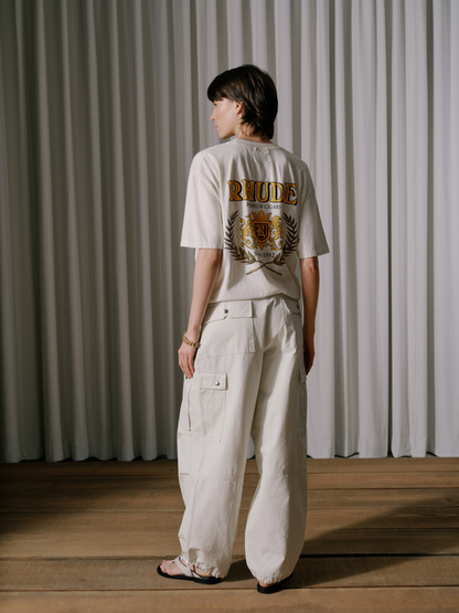 Model wearing the off-white parachute pants with a white tee printed with a gold RHUDE crest, back view