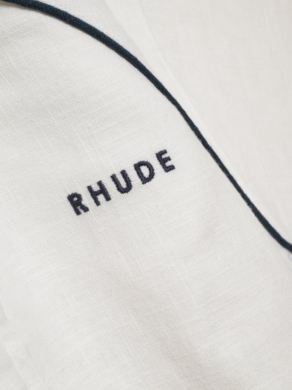 Detail of the textured white fabric with navy piping and a navy embroidered RHUDE logo on the track jacket