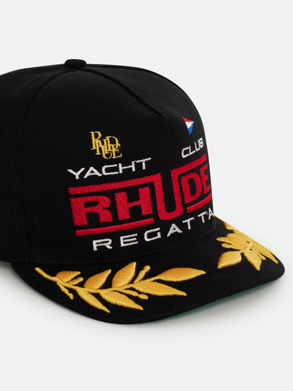 Black Regatta cap with red RHUDE “Yacht Club” embroidery, gold laurel brim and green underbrim, three-quarter view