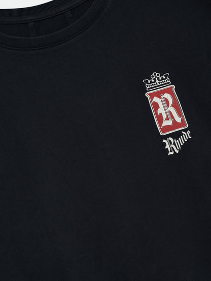 Close-up of the crowned red R badge and white gothic Rhude logo on the chest of the vintage black tee