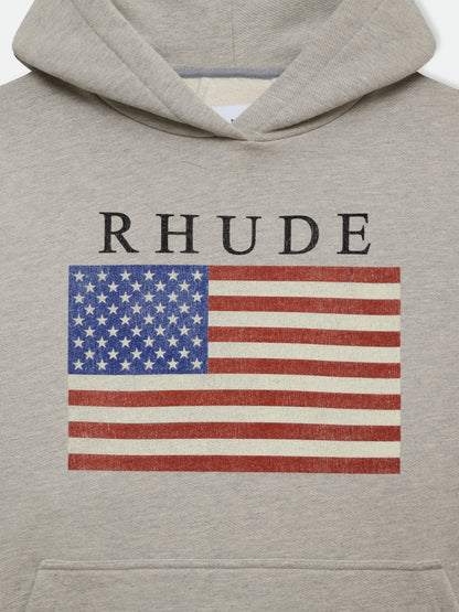 Close-up of the black RHUDE lettering and US flag print above the pouch pocket on the heather grey hoodie