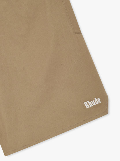 Close-up of the white Rhude logo on the curved hem of the khaki twill shorts
