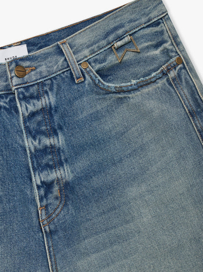 Close-up of the brass button fly, chevron hardware and white RHUDE label on the faded indigo denim shorts