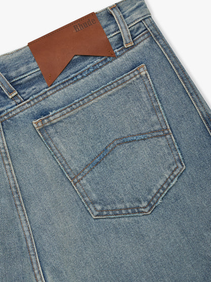 Close-up of the brown Rhude waistband patch and chevron-stitched back pocket on the faded indigo denim shorts