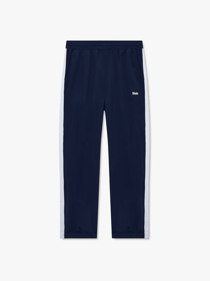 Navy track pants with white side stripes, cuffed hems and a small white Rhude logo at the hip, front view