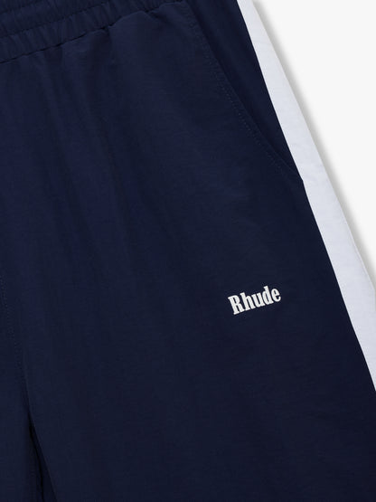 Close-up of the white Rhude logo, elastic waistband and white side stripe on the navy track pants