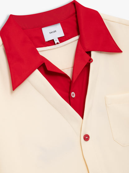 Angled close-up of the red layered collar, Rhude neck label and red buttons on the cream bowling shirt