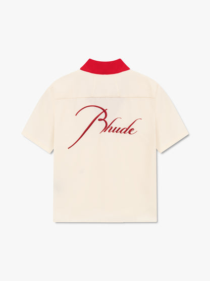 Cream bowling shirt with a red collar and large red script Rhude embroidery across the back, back view