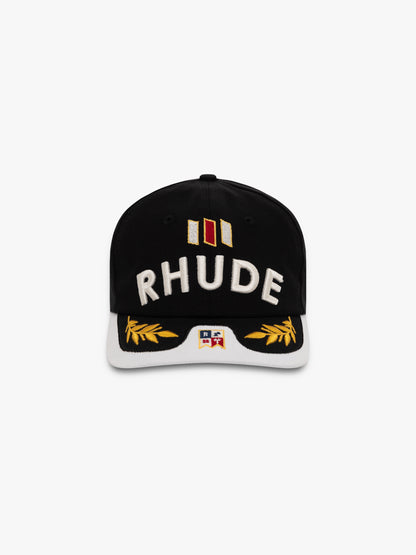Black cap with a white brim, raised white RHUDE embroidery, gold laurel leaves and a small flag patch, front view