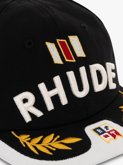 Close-up of the raised white RHUDE embroidery, red striped badge, gold laurels and flag patch on the black cap
