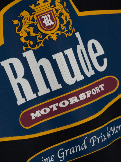 Close-up of the cracked Rhude Motorsport print with a crowned R shield and gold lions on the black hoodie