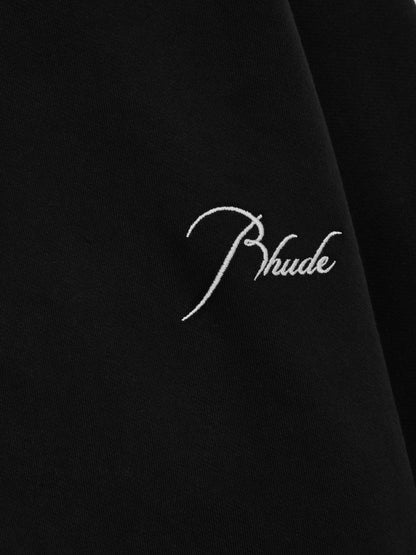Close-up of the white script Rhude embroidery on the black full-zip hoodie