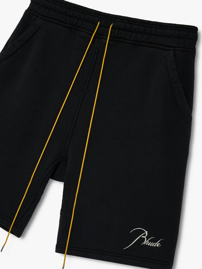 Angled close-up of the tan drawcords, side pocket and white script Rhude embroidery on the black sweat shorts