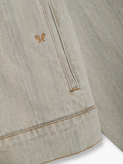 Close-up of the small tan embroidered motif beside the welt hand pocket on the liberty grey denim jacket