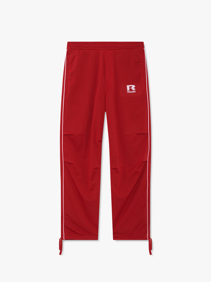 Red mesh track pants with white side piping, knee pleats, ankle ties and a white R Rhude logo, front view