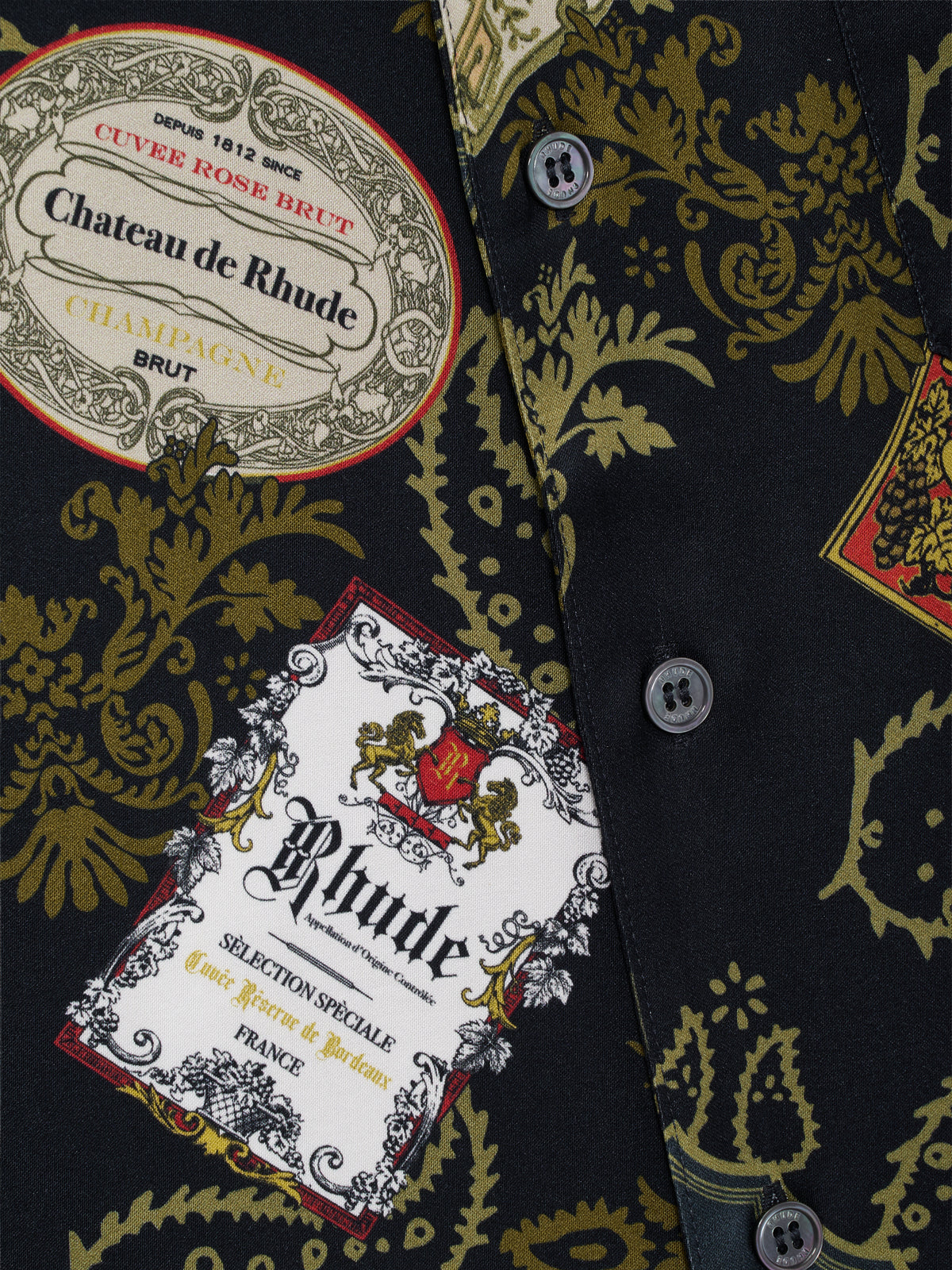 Close-up of the “Chateau de Rhude” champagne label and gold paisley print beside the buttons on the black shirt