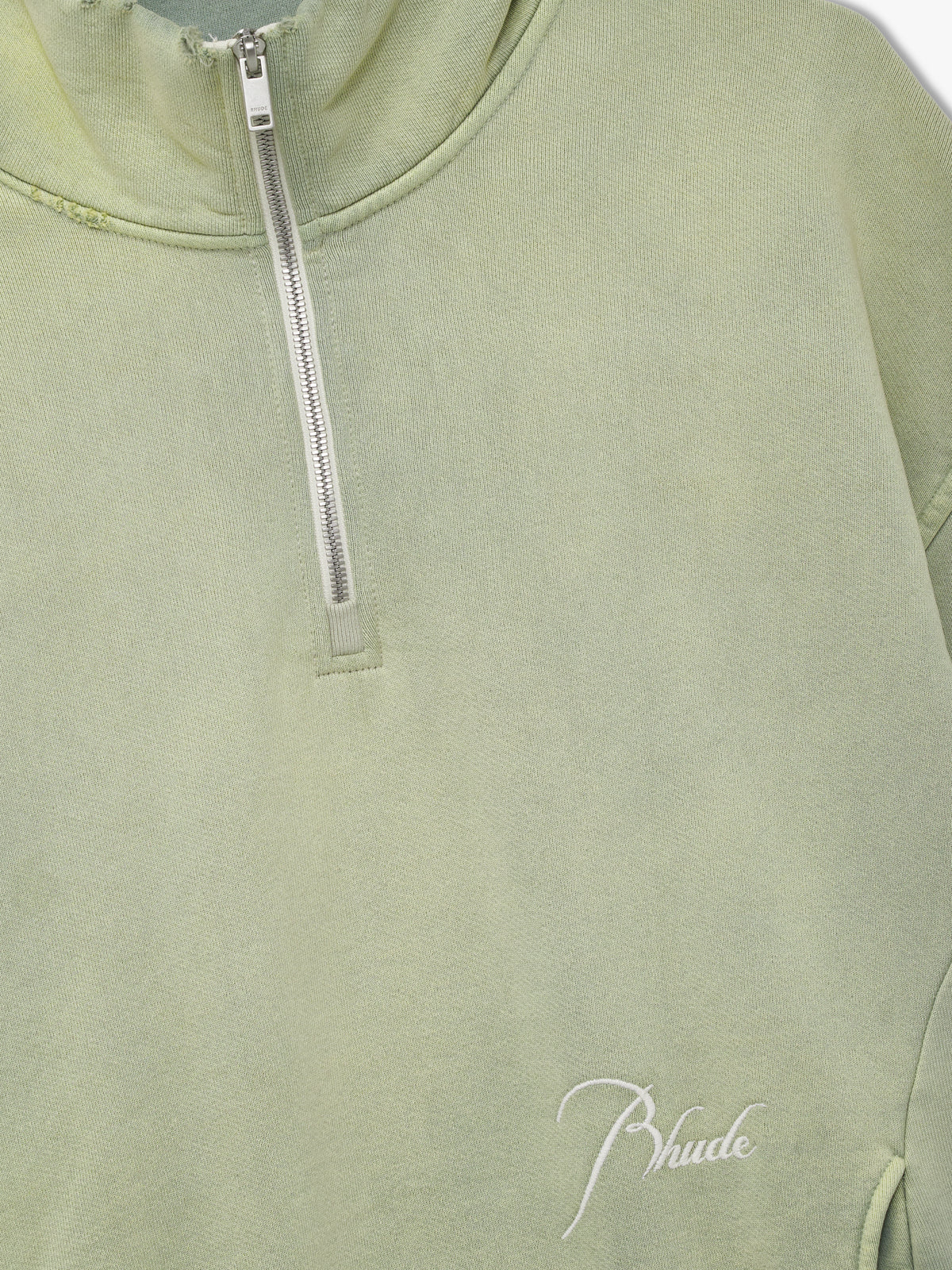 Close-up of the silver zip, distressed collar and white script Rhude embroidery on the washed seafoam quarter zip