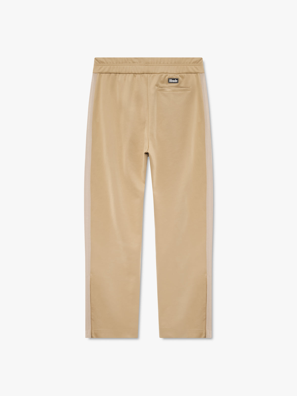Tan track pants with tonal side stripes, a back welt pocket and a black Rhude logo patch at the waist, back view