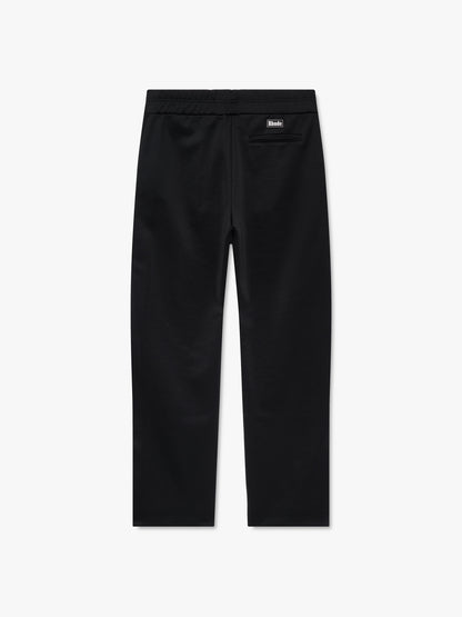Black track pants with pintucked legs, a back welt pocket and a black Rhude logo patch at the waist, back view