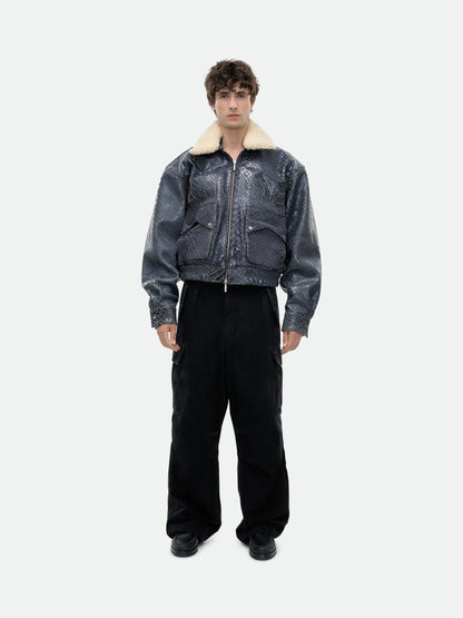 Model wearing the navy crocodile-textured pilot jacket with a cream collar and black wide-leg trousers, front view
