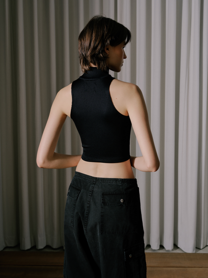 Model wearing the black ribbed knit sleeveless top with a high collar and black pants, back view