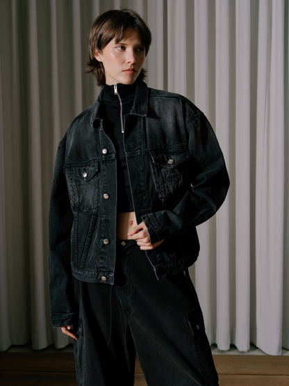 Model wearing the black ribbed turtleneck zip top under a washed black denim jacket with black cargo trousers