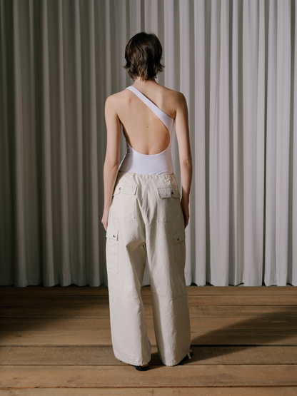 Model wearing the off-white parachute pants with a white open-back one-shoulder bodysuit, back view