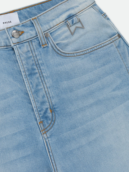 Angled close-up of the button fly, RHUDE waistband label and metal chevron hardware on the coin pocket of the jeans