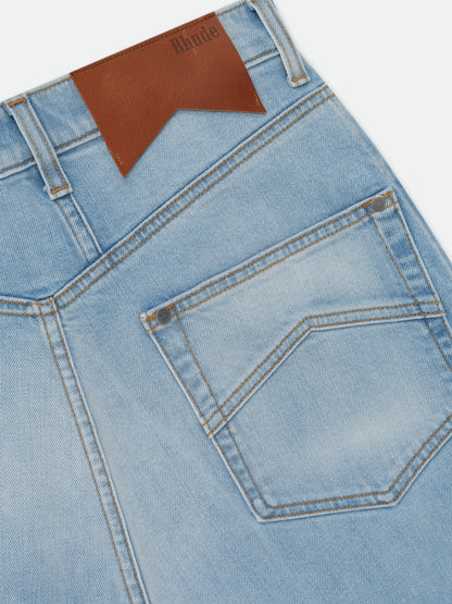 Angled close-up of the brown Rhude debossed back patch and chevron-stitched back pocket on the light-wash jeans
