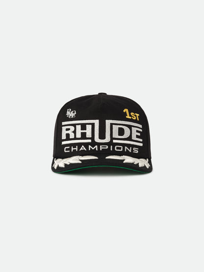 Black cap with white RHUDE “Champions” embroidery, a gold “1ST” and white laurels on the brim, front view